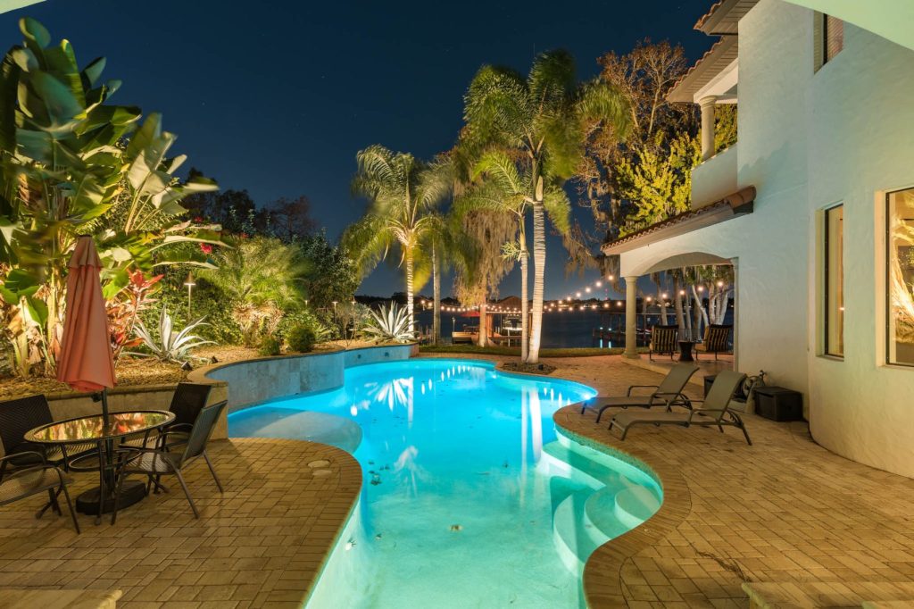 pool lighting and bistro lighting outside home with pool furniture